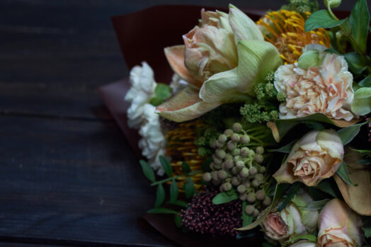 Blombukett med blandade blommor och gröna blad på ett mörkt bord.