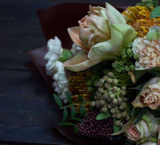 Blombukett med blandade blommor och gröna blad på ett mörkt bord.